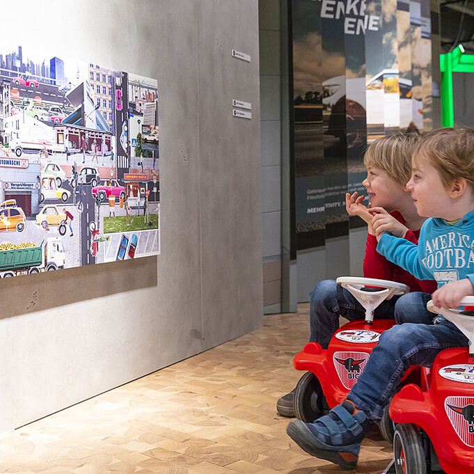 Bunte Bild Collage im Stil des Corporate Designs der Ausstellung hängt an der Wand und wird von zwei Kindern begutachtet